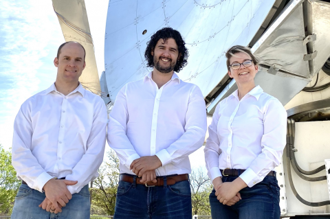 Three people in white shirts stand in front of a large, shiny telescope.