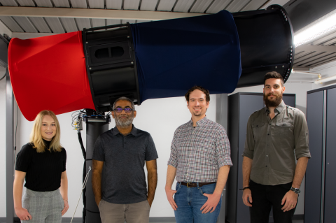 Four people stand in front of a large red and blue telescope.