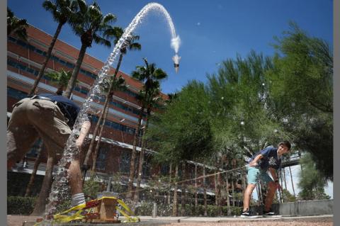 A student pulls on a rope to launch a bottle rock, which is making a big arc through the sky and back toward the ground.