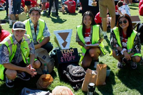 Two young men and two young women wearing Hawaiian shirts and bright yellow vests kneel for a photo next to their solar oven, a cardboard and aluminum foil device labeled with their group name: "Team Hot Stuff."