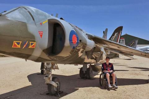 Alex Spartz, an engineering student and wheelchair user, sits in front of an airplane at the Pima Air and Space Museum.