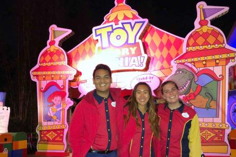 Three smiling people in Disney uniforms in front of the Toy Story Mania! attraction.