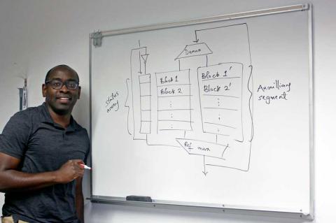 Tosiron Adegbija stands at a whiteboard with a diagram of computer memory caching written on it in black marker