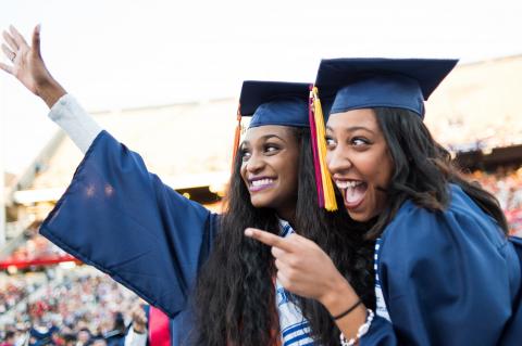 Two women wearing caps and gowns pose for a photo at graduation.