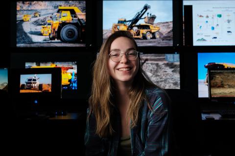 a student poses in front of several screens running mining software