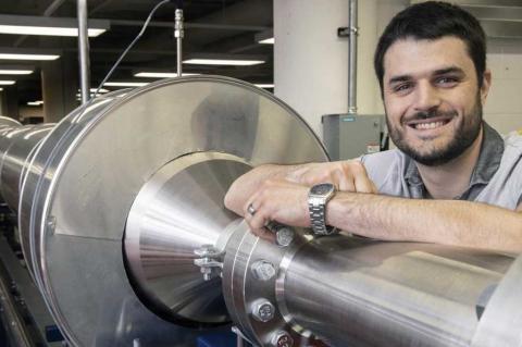 Alex Craig smiles and rests his arm on a 104-foot silver wind tunnel