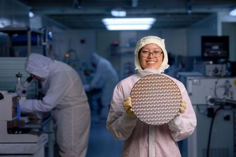 A student in a gown holds a test wafer in the clean room