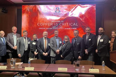 a large group of panelists poses in a conference setting