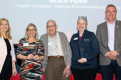 Five people pose with two award statues