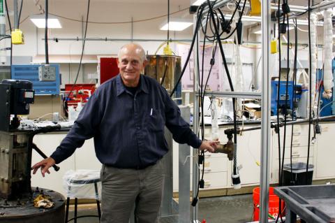 Don Gervasio, wearing a long-sleeved blue shirt, stands between a pump and pipe in a laboratory with tubes hanging in the background