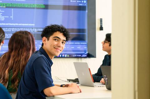 a group of students in a classroom looking at a large monitor