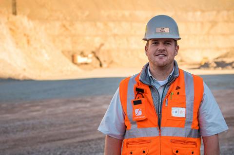 UA mining engineering alumnus Jeff Tysoe stands at the bottom of an open pit mine in a hardhat and orange safety vest 