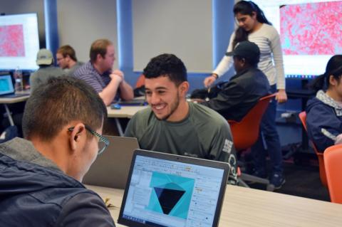 A students, seen from behind, looking at a rending of a mine plan on his laptop. He is in a classroom, and other students can be seen in the background.