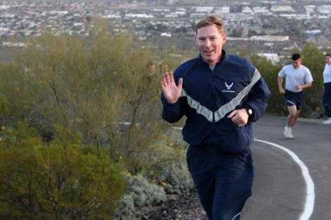Ryan Raettig smiling and waving as he runs up Tumamoc Hill.