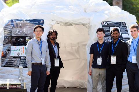 Students stand in front of the tall sandbag structure outdoors