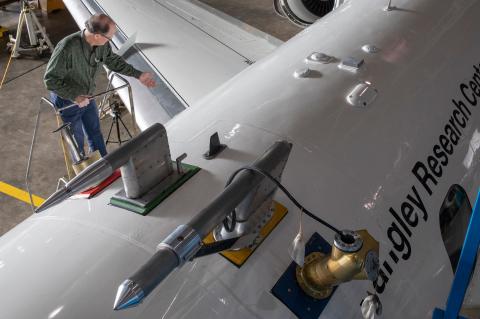 A photo shot from above of a man at the top of a ladder next to a large white airplane, which says "Langley Research Center" on the side.