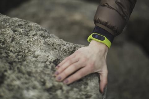 A close-up of a hand resting on a rock. There is a green smartwatch on the wrist.