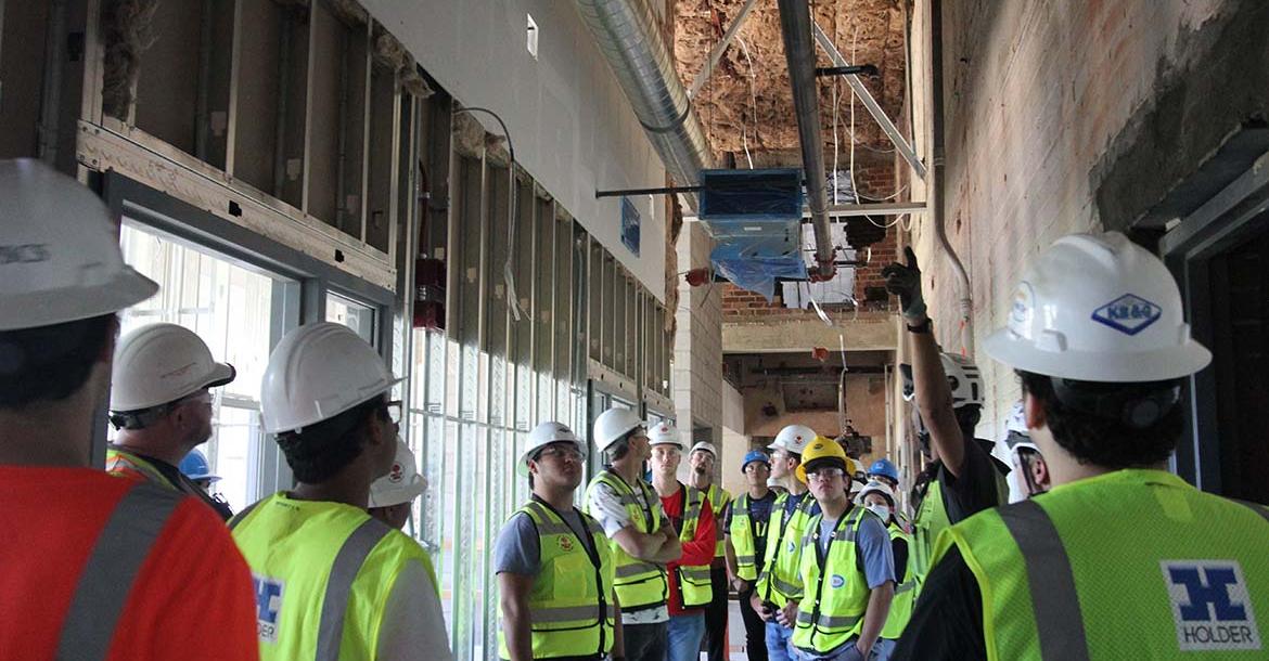 a group of students in hard hats tour an indoor construction site
