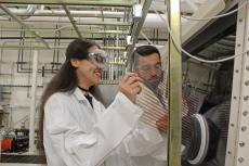 Two students wearing lab coats and goggles in a lab.