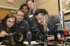 Five students lean over a display of optical equipment