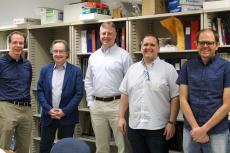 Five men pose for a photo in front of a bookshelf