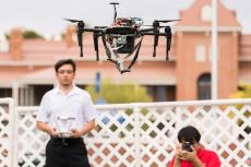 A student in a white polo shirt flies a tethered drone outside Old Main at Engineering Design Day