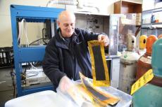 Dominic Gervasio smiles while he sifts through a stack of composite membranes, paper-thin black material with transparent yellow borders, about 1.5 feet by six inches.