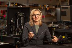 Jennifer Barton in her lab, holding a falloposope, which looks like a thin wire about 1.5 feet long.