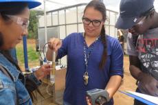 A woman, center, holds a device into a vial of water, while people on either side of her watch.