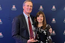 Mike and Sheri Hummel in front of a UA backdrop with a glass award