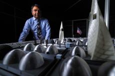 A man in a blue shirt stands in front of a small-scale table that mimics a lunar base.