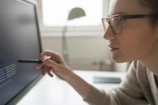 A woman leans over a computer screen, examining lines of code.