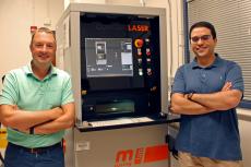 Andrew Wessman and Mohammed Shafae standing next to a 3D printer, which is about two feet wide and a bit taller than them.