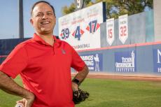 Ricardo Valerdi stands with a baseball and catcher's mitt in a baseball stadium