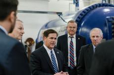 Six men stand next to a blue wind tunnel talking.