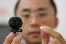 A man holds up a small 3D-printed black sphere in one hand, a penny in the other. The sphere is only about 3 times the size of the penny.