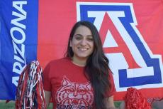 Maira Garcia smiles and holds two pom poms. Behind her is the University of Arizona Block A logo.