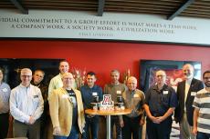 A group of 11 stands around a table holding award medallions