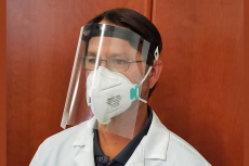 Man wearing a plastic face shield and a white lab coat