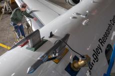 A photo shot from above of a man at the top of a ladder next to a large white airplane, which says "Langley Research Center" on the side.